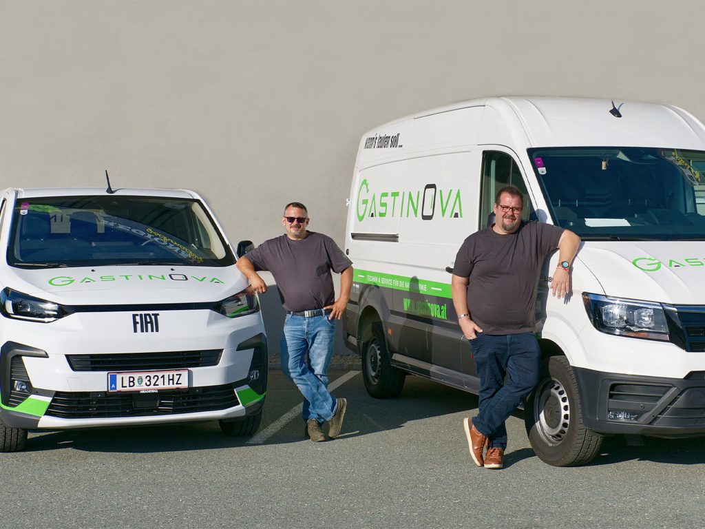 Zwei Firmenautos von Gastinova Gastronomieservice, davor stehen die zwei Techniker